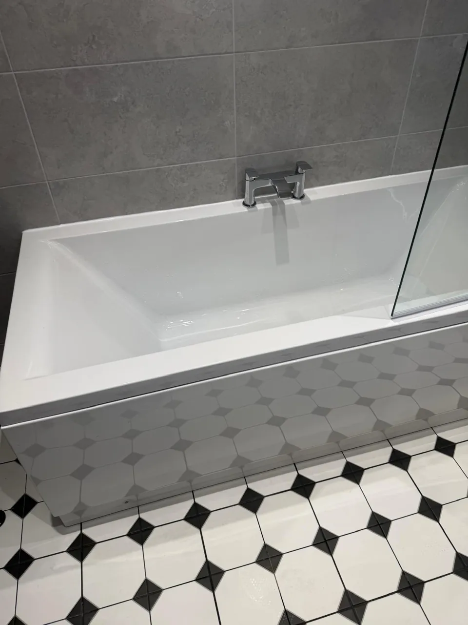 White fitted bath beside a black-and-white patterned floor
